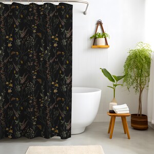 May include: A black shower curtain with a botanical pattern featuring wildflowers in shades of yellow, brown, and green. The curtain is hanging in a bathroom with a white tub and a small wooden stool.