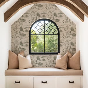 May include: A cozy window seat with a black arched window and a scenic wallpaper. The seat features beige cushions and pillows, with white storage drawers below. Wooden beams frame the window, creating a warm and inviting space.