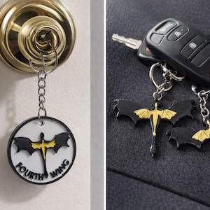 May include: Keychains with a black and gold dragon design. One keychain is attached to a key in a door lock, and the other two are next to a car key fob. The keychains have a circular design with the words "FOURTH WING".