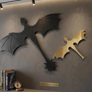 May include: Two metal dragon wall art pieces. One is black, the other is gold. The black dragon has a long tail with a starburst design. The gold dragon is smaller. The text on the plaque reads "The Black Dread & The Golden Wing."