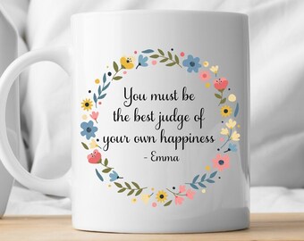 May include: A white ceramic mug featuring a colorful floral wreath design surrounding the black printed text: You must be the best judge of your own happiness - Emma. The mug has a curved handle and a smooth, glossy finish.