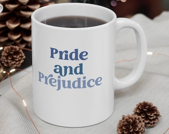 May include: White ceramic coffee mug with a blue and white gradient design that says "Pride and Prejudice". The mug is filled with coffee and is sitting on a white surface with a string of lights.
