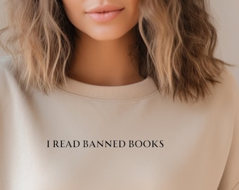 May include: A beige sweatshirt with the text "I READ BANNED BOOKS" in black. The sweatshirt has a crew neck and long sleeves. The image is a close-up of the sweatshirt.