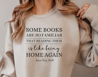 May include: A beige sweatshirt with the text "SOME BOOKS ARE SO FAMILIAR THAT READING THEM is like being HOME AGAIN -Louisa May Alcott" printed on the front.