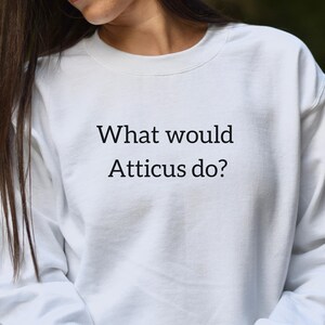 Puede incluir: Sudadera blanca con el texto "What would Atticus do?" impreso en la parte delantera.