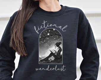 May include: Black sweatshirt with a graphic of a woman reading a book under a starry sky. The text "fictional wanderlust" is printed on the sweatshirt.