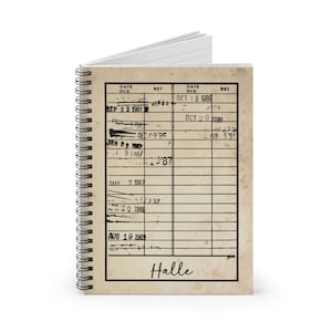 May include: A vintage-style notebook with a brown cover and a spiral binding. The cover has a grid pattern with dates and return dates written in black ink. The notebook is labeled "Halle" at the bottom.