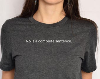 May include: Dark grey crew neck t-shirt with the white text "No is a complete sentence". The shirt is made of a soft, heathered fabric. The image shows the upper torso of a person wearing the t-shirt.