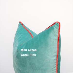 May include: A square mint green velvet throw pillow featuring a vibrant coral pink piped edge. The text Mint Green and Coral Pink is printed on the front of the pillow, indicating the colors of the fabric and the decorative piping trim.
