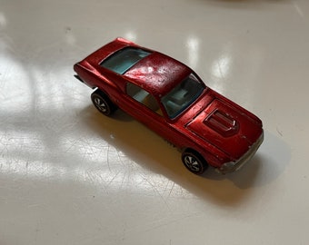May include: A red toy car model of a Ford Mustang with a black hood scoop and black wheels.