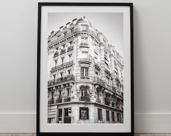 May include: Black and white photograph of a Parisian building with multiple windows and balconies. The building has a corner design and is several stories tall.