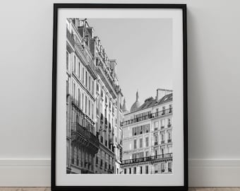 May include: Black and white framed print of Parisian architecture. The image features detailed facades of buildings with balconies and windows, set against a clear sky. The print is displayed in a black frame, adding a classic touch to the artwork.