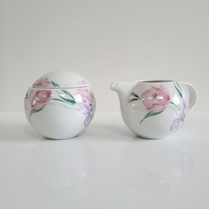 Peut inclure: Un ensemble sucrier et crémier en porcelaine blanche avec un motif floral composé de fleurs roses et violettes. L'ensemble a une forme ronde et une finition brillante.