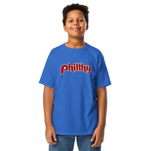 May include: A young person wearing a royal blue t-shirt with the word "philthy" printed in red on the front.