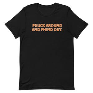 Può includere: T-shirt nero con la scritta "PHUCK AROUND AND PHIND OUT" in arancione con bordo bianco. La maglietta ha maniche corte e scollo tondo. Il tessuto sembra morbido.