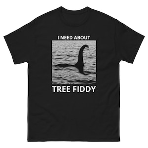 May include: A black short-sleeve t-shirt featuring a square graphic of the Loch Ness Monster in water. Above the image is the white text I NEED ABOUT and below the image is the white text TREE FIDDY. The shirt has a crew neckline.