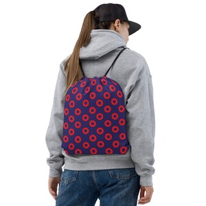 May include: A blue drawstring bag with a red donut pattern. The bag is being worn by a person wearing a grey hoodie and blue jeans.