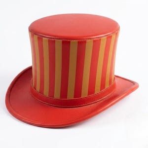 May include: A top hat featuring a flat crown and a wide brim, constructed from red material. The cylindrical body of the hat is decorated with vertical stripes in alternating shades of red and tan, with a solid red band encircling the base.
