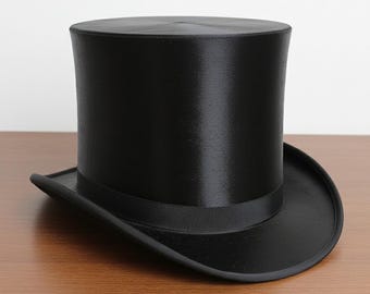 Puede incluir: Un sombrero de copa negro clásico con acabado satinado. El sombrero presenta una copa alta y cilíndrica y un ala ancha y curvada. Una cinta negra rodea la base de la copa. Es un accesorio formal.