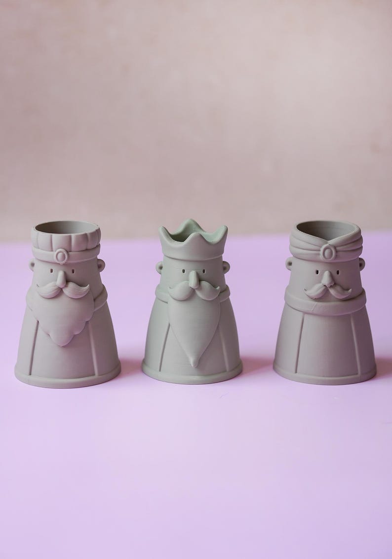 Peut inclure: Trois tasses en c&eacute;ramique gris mat en forme de personnages stylis&eacute;s avec moustaches et barbes. Chaque tasse pr&eacute;sente un couvre-chef distinct : une casquette &agrave; sommet plat, une couronne &agrave; trois pointes et un turban. Visages simplifi&eacute;s.