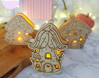 May include: Three wooden mushroom-shaped night lights with warm yellow interior lighting. The mushroom houses have intricate cut-out designs, including windows, doors, and decorative patterns. The text "GLOWVYBE" and "Laserdatei - SVG & PNG" are visible.