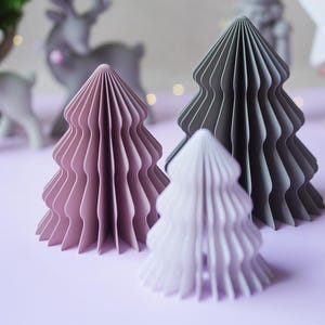 Può includere: Tre alberi decorativi in carta a nido d'ape di varie dimensioni e colori. Un albero è color malva polveroso, uno è grigio antracite scuro e l'albero più piccolo è color lavanda pallido. Ogni albero presenta un design conico a fisarmonica pieghettato.