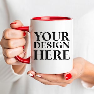 May include: A white ceramic mug with a red rim and handle. The mug has the text "YOUR DESIGN HERE" printed in black.