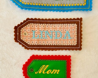 May include: Four colorful felt name tags with scalloped edges. The top tag is blue with "PRE K HIDDEN LAKE" and a large red "K". Other tags read "LINDA", "Mom", and "JENNY".