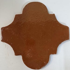 May include: A single, four-pointed, cross-shaped tile with rounded edges and a glossy, solid brown finish. The surface of the tile features a smooth, reflective texture with subtle variations in the glaze, creating a uniform, earthy appearance.
