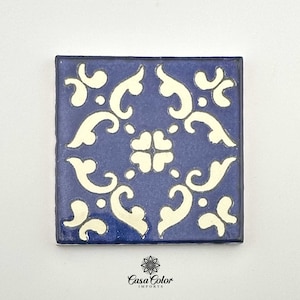 May include: A blue ceramic tile with a white floral pattern. The tile has a square shape and is decorated with a repeating design of stylized flowers and leaves.