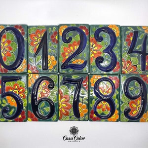 May include: Set of ten ceramic tile house numbers with a green background and colorful floral designs. The numbers are painted in blue and are outlined in black. The numbers are 0 through 9.