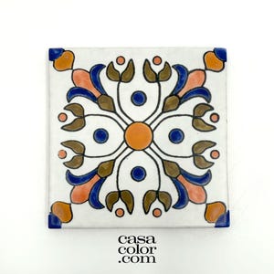 May include: A white ceramic tile with a blue, orange, and brown floral pattern. The tile has a square shape and is decorated with a repeating design of stylized flowers and leaves.