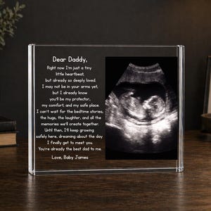 May include: A clear acrylic photo block with a black and white ultrasound image and a heartfelt message to "Daddy." The text reads "Dear Daddy... You're already the best dad to me. Love, Baby James."