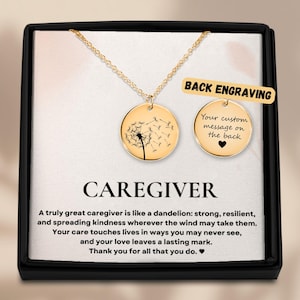 May include: Gold-colored necklace with two round pendants. One pendant features a dandelion design, the other has space for a custom message. The box reads "CAREGIVER" and includes a message about caregivers.