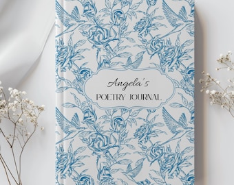 Può includere: Un diario di poesia con copertina rigida con un motivo floreale e di uccelli blu su sfondo bianco. La copertina del diario presenta il testo "Angela's POETRY JOURNAL" in una cornice decorativa.