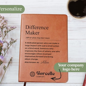 May include: A brown leather journal with the words "Difference Maker" and its definition printed on the cover. The journal includes the name "Alex" and the company logo. A cup of coffee and flowers are in the background.