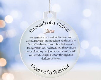 May include: A white round ornament with the text "Strength of a Fighter" and "Heart of a Warrior" in black lettering. The name "Jason" is written in red lettering. The ornament has a silver string attached to it.