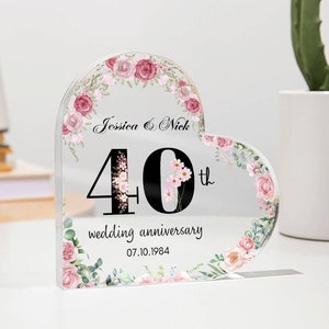 Könnte beinhalten: Eine herzförmige, transparente Acryl-Plakette mit floralem Design und dem Text "Jessica & Nick 40. Hochzeitstag 07.10.1984".