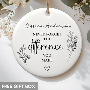 May include: White ceramic ornament with black text and floral illustrations. The text reads "Jessica Anderson Never Forget The Difference You Make" with a heart symbol at the bottom.