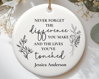 Op de afbeelding: Witte keramische ornament met zwarte tekst en bloemillustraties. De tekst luidt "Vergeet nooit het verschil dat je maakt en de levens die je hebt aangeraakt." De naam "Jessica Anderson" staat onder de tekst gedrukt.