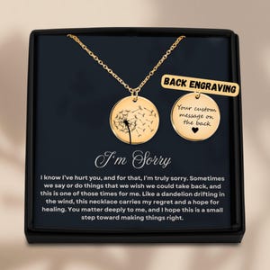 May include: Gold-colored necklace with a round pendant featuring a dandelion design. The necklace is presented in a black box with the words "I'm Sorry" and a message. A second pendant shows "Back Engraving".