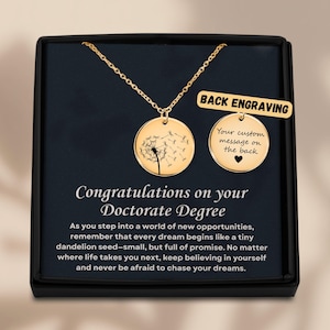 Può includere: Collana dorata con due ciondoli rotondi. Uno presenta un design di dente di leone, l'altro è personalizzabile. La scatola recita "Congratulazioni per il tuo dottorato".