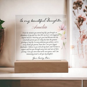 May include: A clear glass plaque with a wooden base, featuring a floral design and a heartfelt message to a daughter named Amelia. The message expresses love, support, and pride in her achievements. The text reads: "To my beautiful Daughter Amelia From the moment you entered my life, you brought an abundance of joy and love that fills my heart with happiness beyond measure. Watching you grow and blossom into the remarkable person you are today has been the greatest privilege of my life. In every milestone you achieve, and in every dream you pursue, know that I am your biggest cheerleader. I believe in you with all my heart, and I'm here to support and love you through every twist and turn of life's journey. I love you more than words can express, and I am immensely proud to call you my daughter. Your loving Mom"