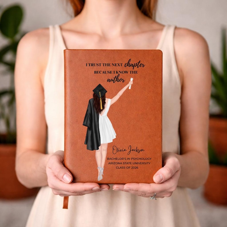 May include: A brown leather-bound journal with the text "I TRUST THE NEXT chapter BECAUSE I KNOW THE author" and a graduation-themed illustration. The journal also includes the name "Olivia Jackson", degree, university, and graduation year.