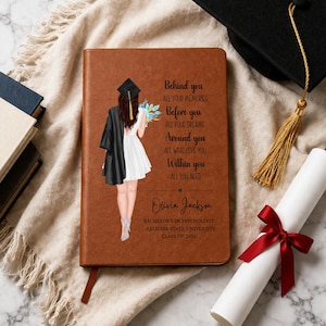 May include: A brown leather-bound journal with a graduation theme. The cover features an illustration of a graduate and text. A graduation cap, tassel, and diploma with a red ribbon are also visible.