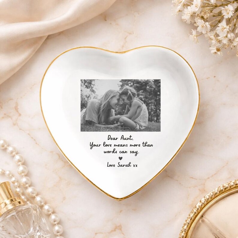 May include: A heart-shaped white ceramic trinket dish with a gold rim, featuring a black and white photo of two people. The dish has the text "Dear Aunt. Your love means more than words can say. Love Sarah xx."