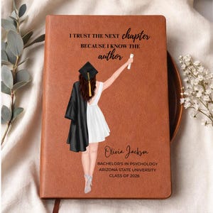 May include: A brown leather-bound journal with the text "I TRUST THE NEXT chapter BECAUSE I KNOW THE author." Features a graduation illustration and the name "Olivia Jackson." Includes "Bachelor's in Psychology, Arizona State University, Class of 2026."