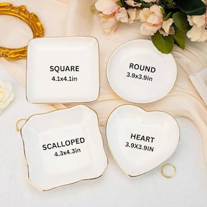 May include: Four white ceramic trinket dishes in square, round, scalloped, and heart shapes. Each dish has gold trim. The square dish is 4.1 x 4.1 inches, the round and heart dishes are 3.9 x 3.9 inches, and the scalloped dish is 4.3 x 4.3 inches.