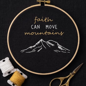 Può includere: Un telaio da ricamo nero con la scritta "faith can move mountains" ricamata in filo d'oro e un motivo montuoso. Include rocchetti di filo e forbici dorate.