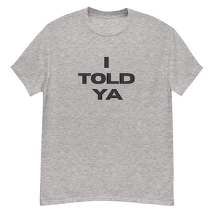 Puede incluir: Una camiseta gris jaspeada con el texto "I TOLD YA" impreso en negro.